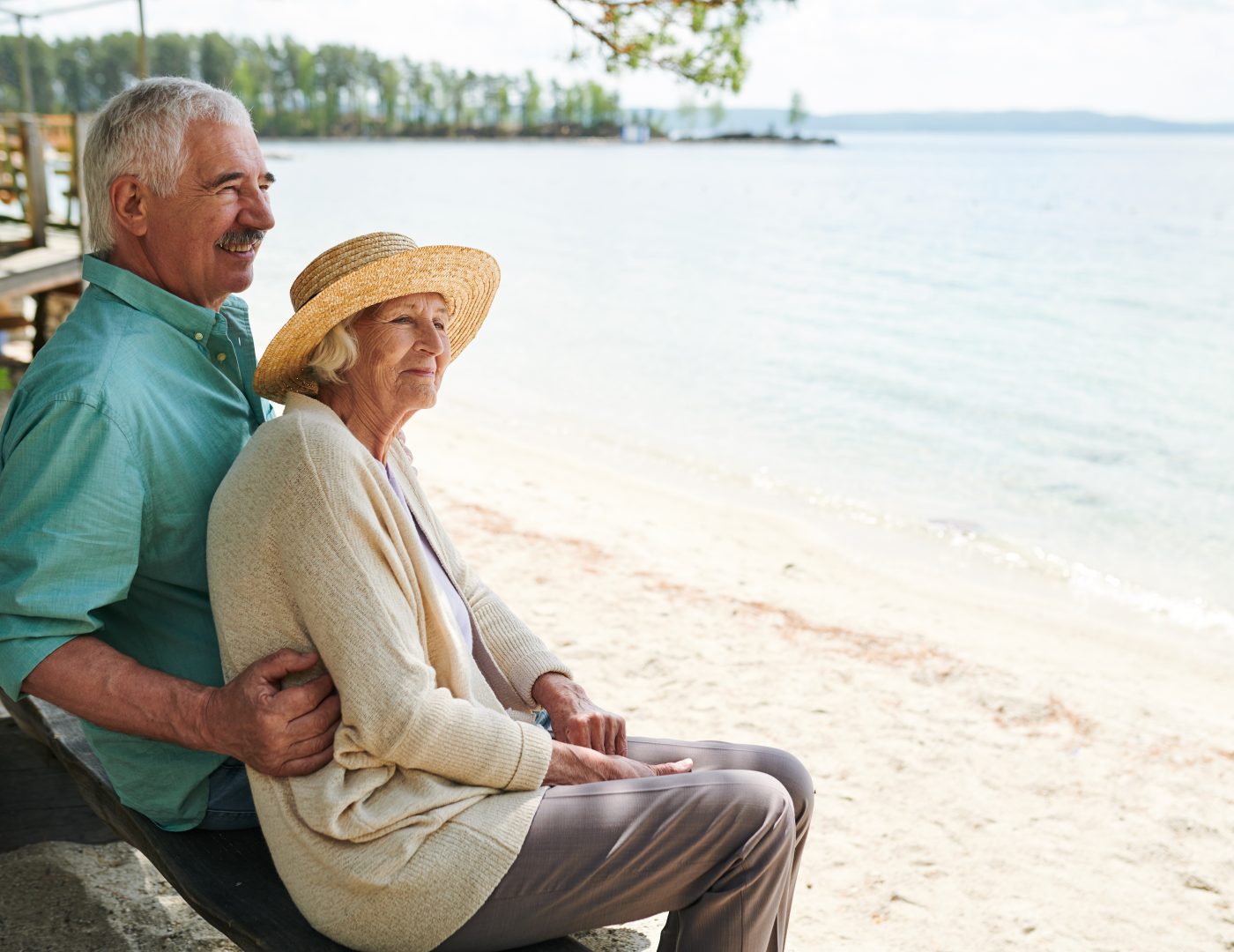 Senior romantic man and woman sitting on the beach by lake, enjoying rest and the weather